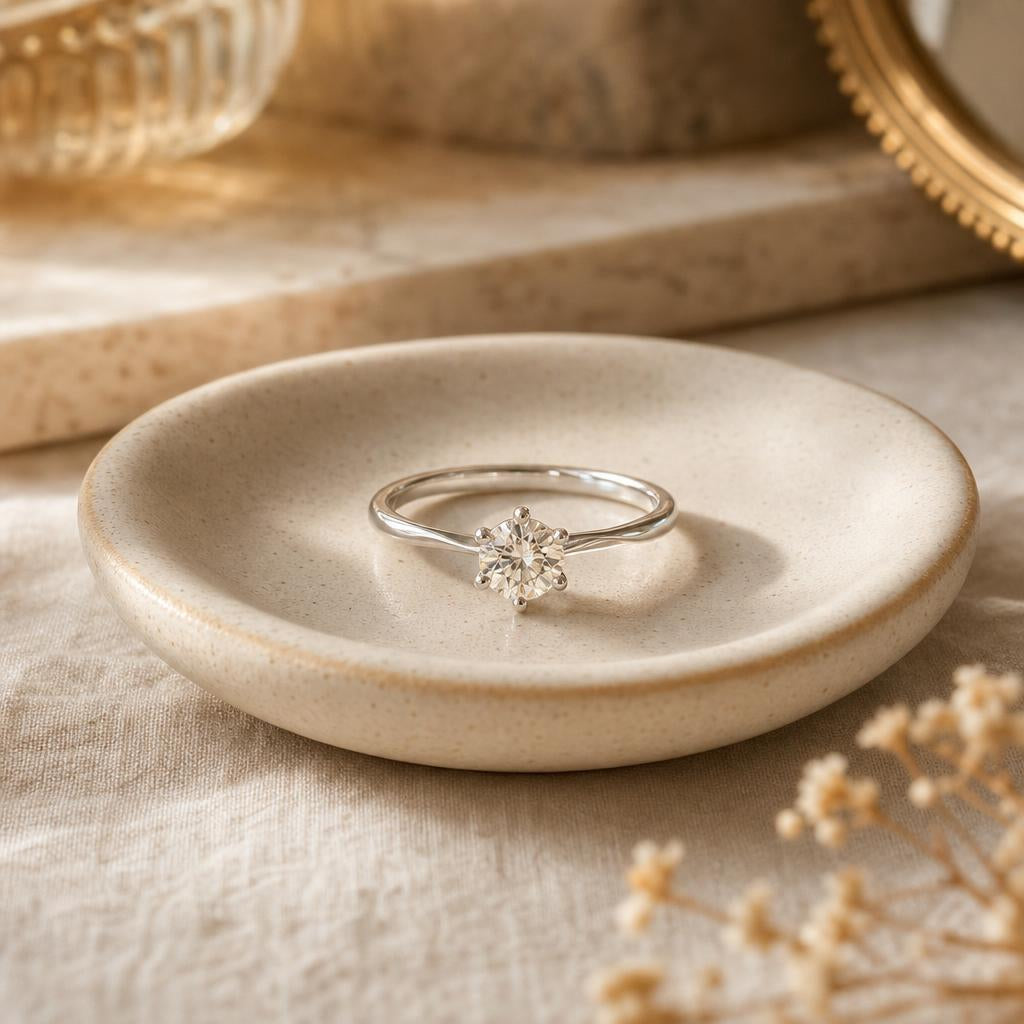 A single sparkling ring resting centered on a ceramic dish in warm light