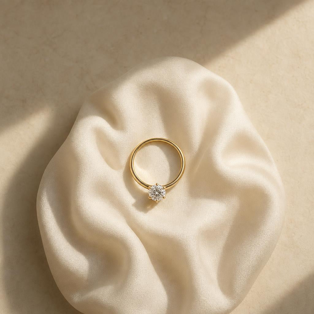 Single solitaire ring resting alone on soft ivory fabric, warm minimal styling