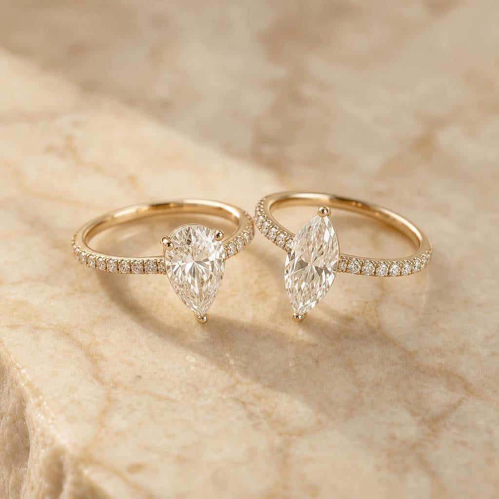 Two elegant rings side by side on cream marble — pear and marquise cut stones