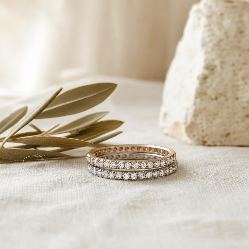 Two stacked sparkling eternity bands on cream linen beside dried olive sprig