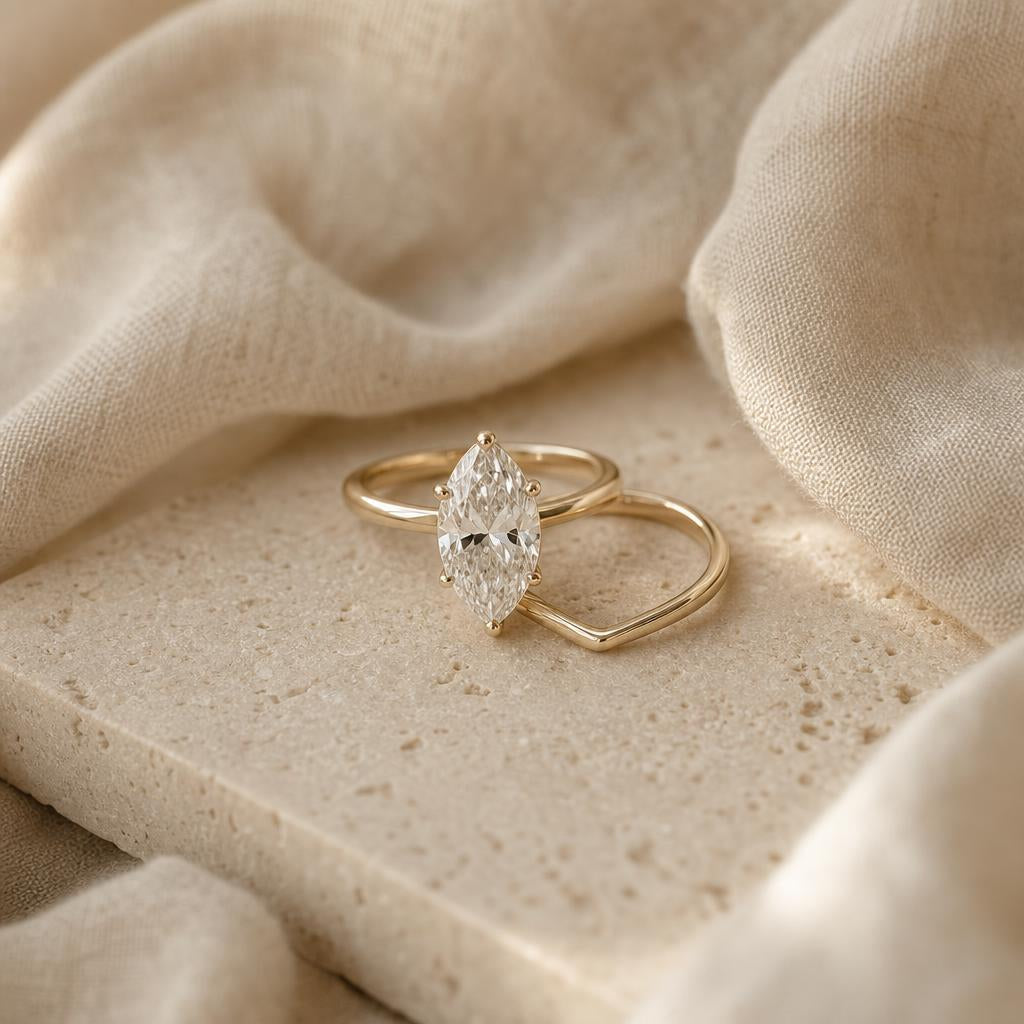 Marquise-shaped ring beside a curved wedding band on warm stone