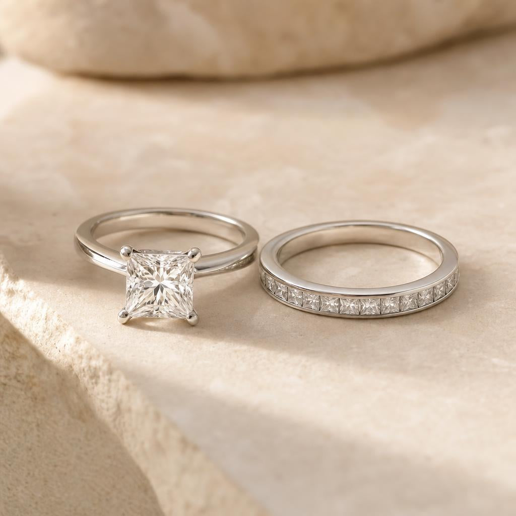 Princess cut solitaire ring beside a slim flat diamond eternity band on warm cream stone