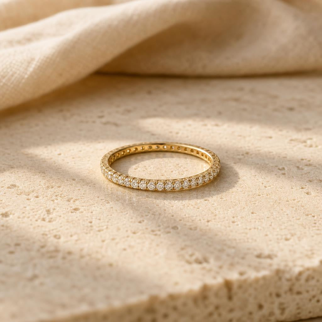 Delicate pavé eternity ring centered on a warm cream stone surface