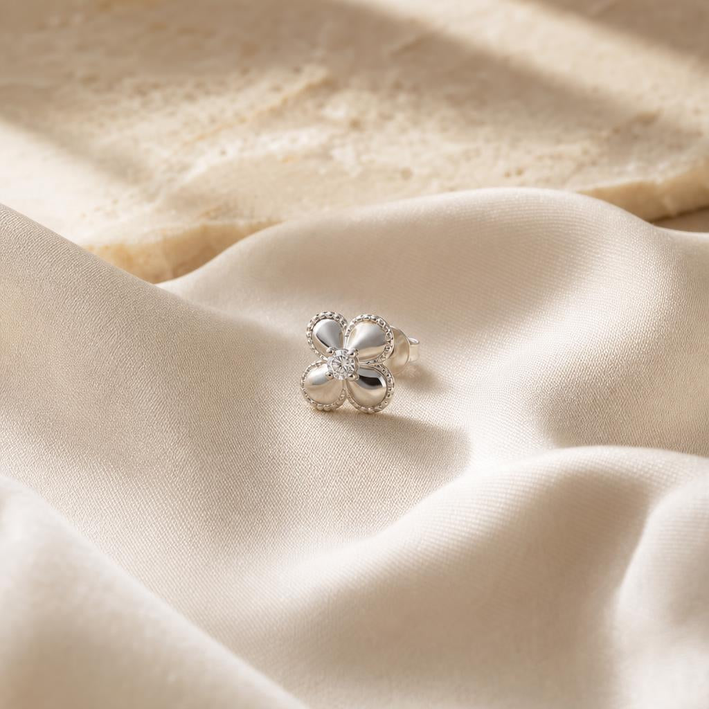 Single sterling silver stud earring centered on warm cream silk fabric