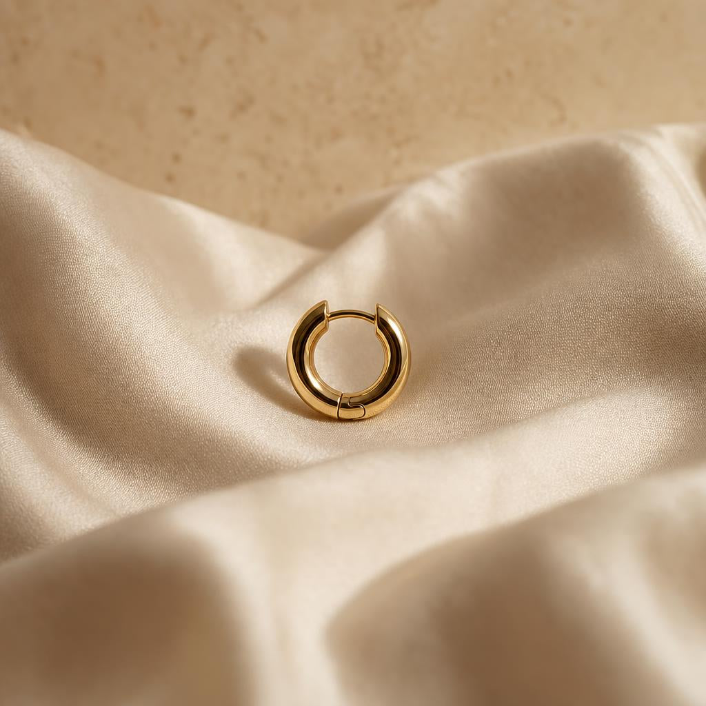 Small silver hinged hoop earring resting on cream silk fabric