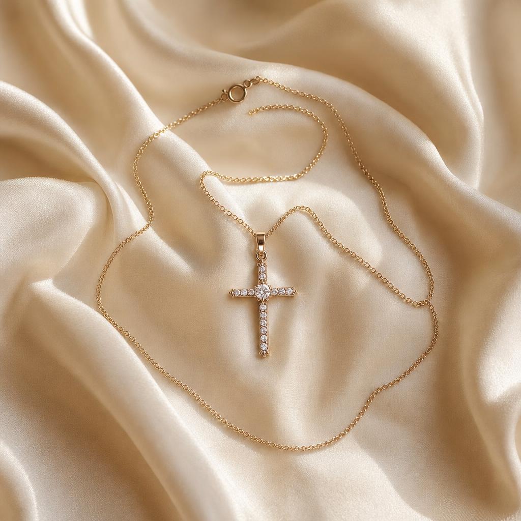 Delicate cross pendant necklace laid on soft cream silk fabric
