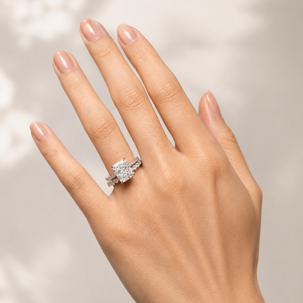 A close-up of a hand wearing a silver-toned ring with a large clear gemstone, photographed against a soft light beige background with subtle shadow patterns.